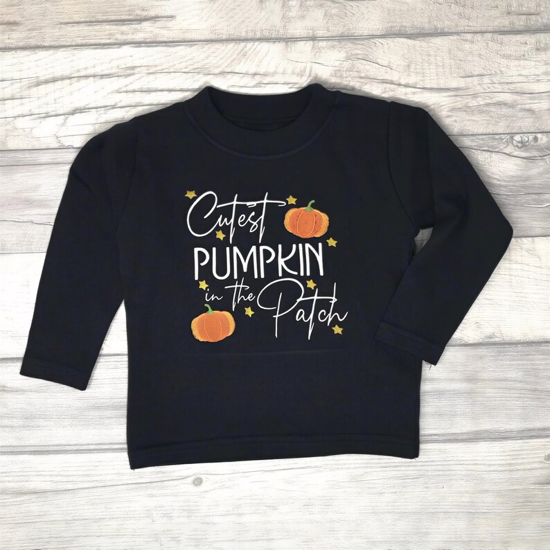 Long sleeve black t-shirt embroidered with black text reading Cutest Pumpkin in the Patch and  orange pumpkins and little yellow stars.