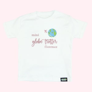 White tshirt embroidered with the phrase mini globe trotter  name and an embroidered earth with an airplane circling it.