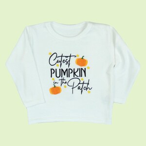 Long sleeve white t-shirt embroidered with black text reading Cutest Pumpkin in the Patch and  orange pumpkins and little yellow stars.