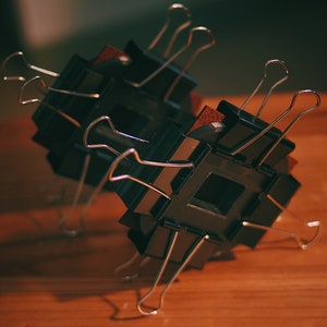 May include: Two black square frames with silver binder clips attached to them. The frames are stacked on top of each other and are sitting on a wooden surface.