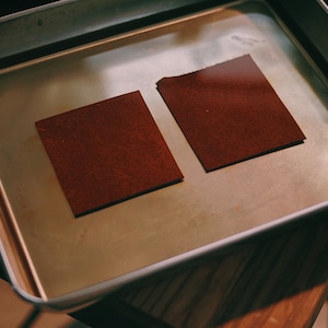 May include: Two brown leather squares submerged in a metal tray filled with water.