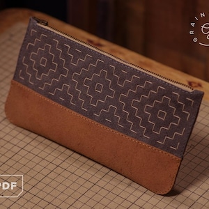 Peut inclure: Une pochette rectangulaire à fermeture éclair présentant un design bicolore avec une section supérieure gris foncé ornée d'un motif géométrique cousu de couleur claire et une section inférieure marron clair unie avec une fermeture éclair.