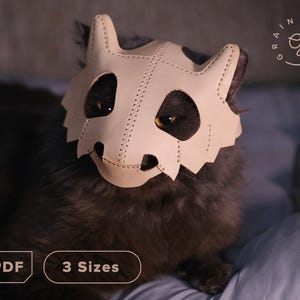 May include: A light-colored leather cat mask with a stitched design, worn by a gray cat. The mask has eye and mouth openings. The image includes the text "PDF" and "3 Sizes". The mask is a unique pet accessory.