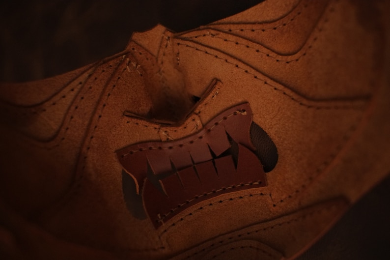 Pu&ograve; includere: Primo piano di una maschera in pelle marrone con un design cucito. La maschera ha un ritaglio a forma di bocca con una fodera in pelle marrone.