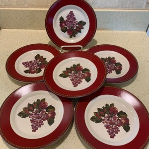 May include: Set of six white ceramic dinner plates with a red rim and a grape and apple design.