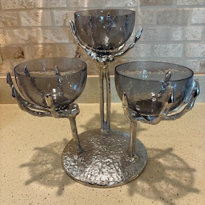 May include: A silver metal three-tiered serving stand with a skeletal hand design. Each tier has a clear glass bowl.