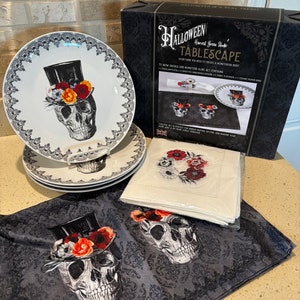 May include: Halloween Harvest Green Studio Tablescape set with four porcelain plates, four ceramic napkin rings, four plastic placemats, and four fabric napkins. The plates and napkins feature a skull design with a top hat and flowers.