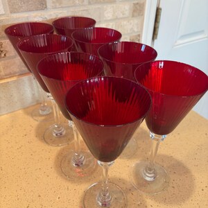 May include: Set of eight red wine glasses with a fluted design. The glasses are clear with a red tint and have a long stem.