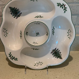 May include: White ceramic Christmas-themed serving dish with a central dip bowl and four smaller bowls around it. The dish is decorated with green holly leaves and red berries, and features a small Christmas tree design in each of the bowls.