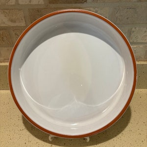 May include: A white ceramic baking dish with a brown rim. The dish is round and has a smooth surface.