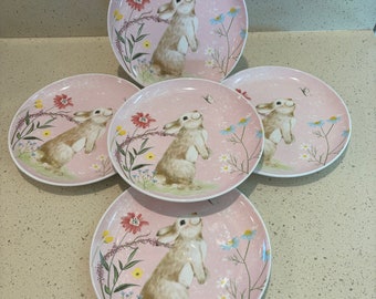 May include: Set of five pink ceramic salad plates with a floral design and a bunny rabbit illustration. Each plate features a different bunny rabbit pose.
