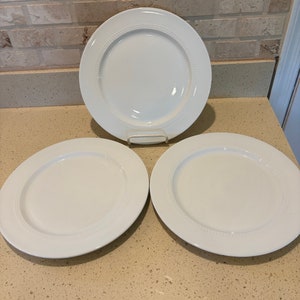 May include: Three white ceramic dinner plates with a raised rim and a beaded edge.