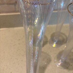 Puede incluir: Un juego de copas de champ&aacute;n iridiscentes con borde dorado. El vidrio transparente presenta un dise&ntilde;o texturizado y ondulado que atrapa la luz, creando un efecto arco&iacute;ris. La cristaler&iacute;a es elegante y adecuada para ocasiones especiales.