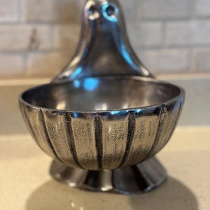 May include: A silver-colored decorative bowl with a ghost-like design. The bowl has a fluted exterior and sits on a pedestal base. The ghost-shaped top adds a unique, spooky touch to the bowl's design.