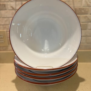 May include: A stack of five white ceramic bowls with a brown rim. The bowls are nested together.