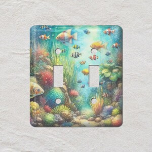 May include: A decorative double light switch cover featuring an underwater scene. The design includes colorful fish, coral, and aquatic plants in shades of blue, green, yellow, and red. The cover has two rectangular switch openings.