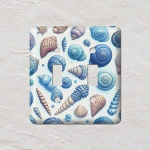 May include: A decorative light switch cover featuring a pattern of various seashells in shades of blue, brown, and tan against a white background. The design includes spiral, conical, and fan-shaped shells, creating a coastal theme.