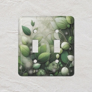 Peut inclure: Un cache-interrupteur décoratif avec un motif botanique. Le couvercle comporte deux ouvertures pour interrupteurs et est orné de diverses nuances de feuilles et de feuillages verts. L'arrière-plan a un aspect doux et texturé.