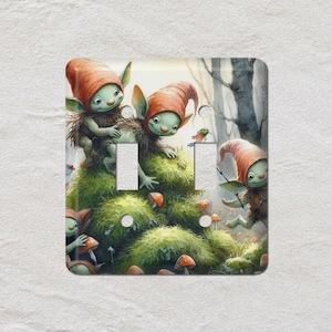 May include: A decorative light switch cover featuring a whimsical illustration of several small, green-skinned creatures with red hats and mossy bodies. They are surrounded by mushrooms and greenery, creating a fantasy forest scene.