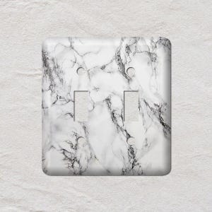 May include: A double light switch cover with a white and gray marble pattern. The cover has two rectangular switch openings and two screw holes. The marble design features gray veining.