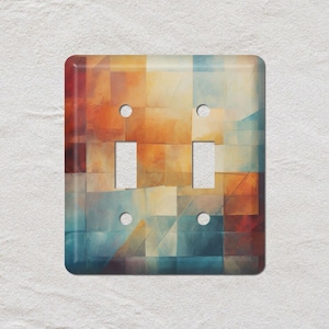 May include: A decorative double light switch cover with an abstract design. The cover features a mosaic of colors including orange, blue, and yellow. The cover has two rectangular switch openings and four screw holes.