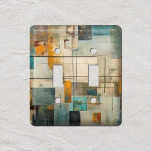 May include: A decorative double light switch cover with an abstract design. The artwork features a mix of rectangular and square shapes in shades of teal, orange, brown, and grey, with black lines. The cover has two switch openings and two screw holes.