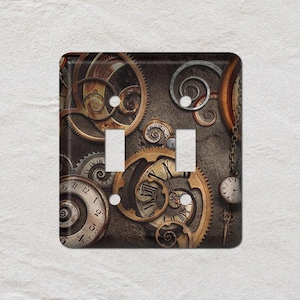 May include: A decorative double light switch cover featuring a steampunk design. The cover showcases a collage of gears, clocks, and spirals in shades of brown, gold, and bronze, creating a vintage aesthetic. The background is a textured, dark brown.