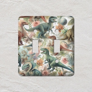 May include: A double light switch cover with a watercolour design of dinosaurs and floral elements. The dinosaurs are in shades of green, brown, and blue, set against a white background with flowers and foliage.