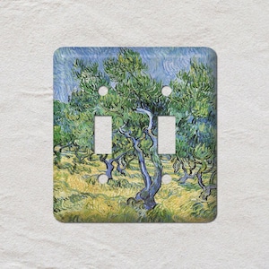 May include: A double light switch cover featuring a print of Vincent van Gogh's "Olive Trees" painting. The artwork depicts olive trees with green foliage and blue trunks against a yellow and blue background. The cover has two switch openings.