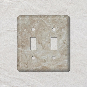May include: A decorative light switch plate with a marble design. The plate has two switch openings and four screw holes. The color is a mix of beige, tan, and brown, with a marbled pattern.