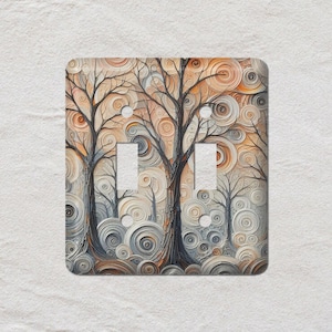 May include: A double light switch cover with an artistic forest design. The image shows bare trees with dark trunks and branches set against a background of swirling, textured patterns in beige, grey, and orange hues.