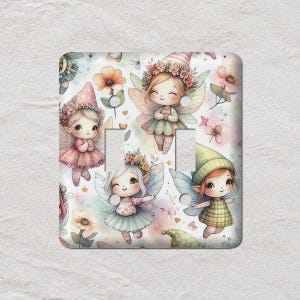 May include: A decorative light switch cover featuring a repeating pattern of whimsical fairies with flower crowns and wings. The fairies are in various poses, set against a soft pastel background with flowers and butterflies. The cover has two switch openings.