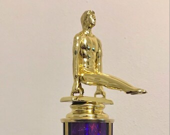 May include: Gold-colored trophy with a figure of a gymnast on top of a purple column. The base is white with a gold plate that says "YOUR WORDS HERE".