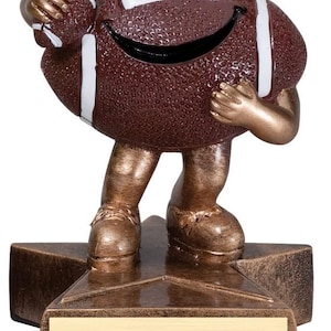 May include: A brown football-shaped trophy with a smiling face, white stripes, and gold-colored arms and legs. The trophy is standing on a star-shaped base with a blank gold plaque.