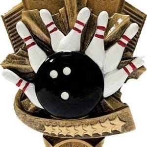 May include: A bowling trophy with a gold and bronze finish. The trophy features a black bowling ball with three white dots, white bowling pins with red stripes, and a star-shaped design. The base has a blank gold plate.