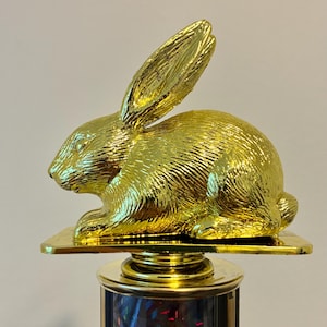 May include: A gold-colored trophy featuring a detailed rabbit figurine. The rabbit is posed in a seated position with its ears erect. The trophy has a black and gold base.