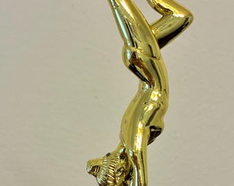 May include: A gold-colored trophy featuring a gymnast in a handstand pose. The figure is detailed and shiny, mounted on a base with red and gold accents. A symbol of achievement.