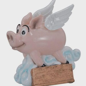 May include: A pink ceramic pig figurine with white wings, perched on a cloud. The pig has a smiling face and is holding a rectangular, bronze-colored sign. The figurine is a whimsical decorative item.