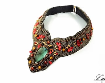 May include: A beaded necklace with a large green gemstone pendant. The necklace is made with gold and red beads and has a floral design.