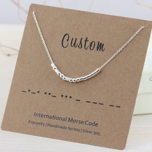 May include: Silver necklace with a custom message in Morse code. The necklace is on a brown card with the text "Custom" and "International Morse Code".