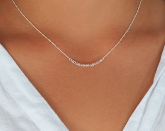 May include: A silver necklace with a delicate chain and a row of small, round beads.
