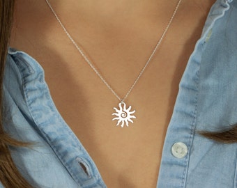 Peut inclure: Un collier en argent avec un pendentif en forme de soleil. Le soleil a un motif en spirale au centre.