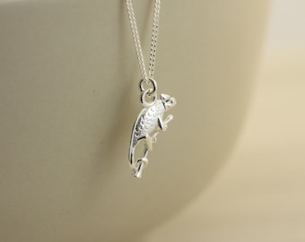 May include: A silver necklace with a detailed chameleon charm. The charm is of a chameleon perched on a branch.