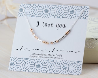 May include: A silver necklace with a silver and rose gold beaded chain that spells out "I love you" in Morse code. The necklace comes with a card that shows the Morse code translation for "I love you".