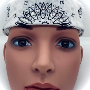 May include: White bandana with black paisley print and a central floral design embellished with sparkling rhinestones. The bandana is folded and worn as a headband.