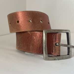 May include: A brown leather belt with a silver buckle. The belt is folded in half and the buckle is on the right side of the image.