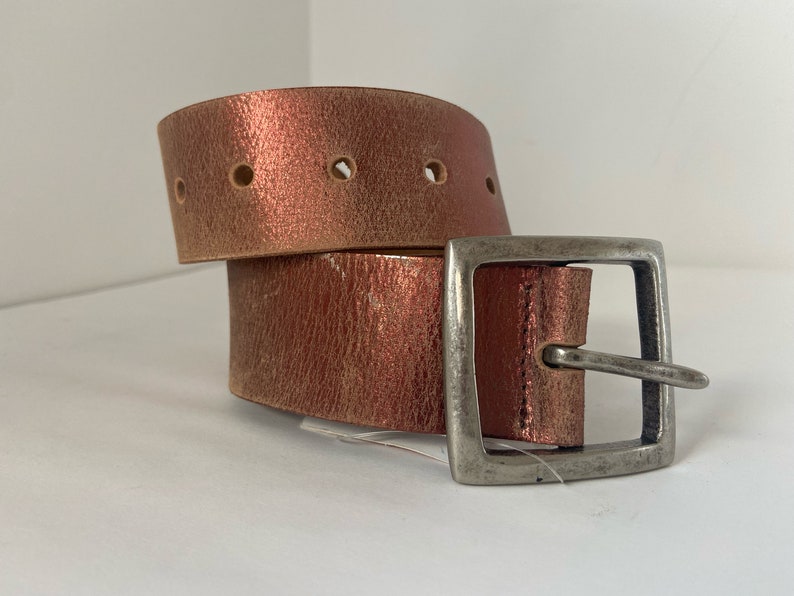 May include: A brown leather belt with a silver buckle. The belt is folded in half and the buckle is on the right side of the image.