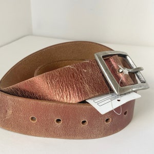 May include: A brown leather belt with a silver buckle. The belt is folded in half and the buckle is on the top of the fold.