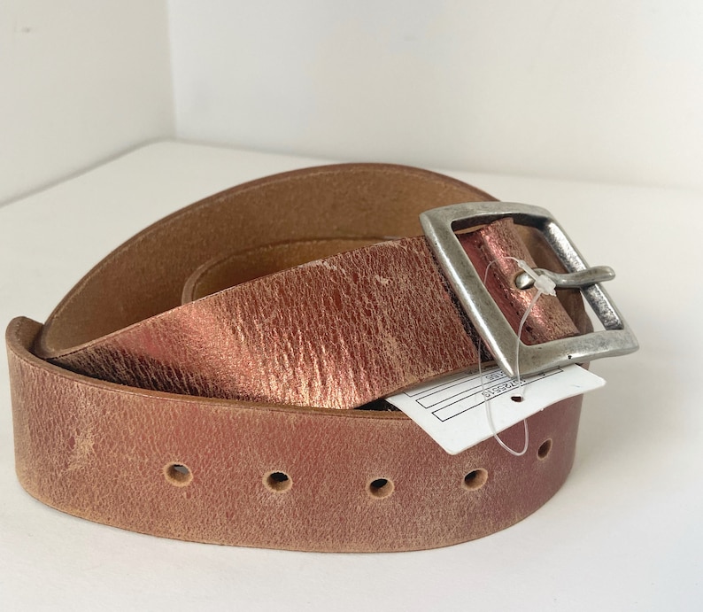 May include: A brown leather belt with a silver buckle. The belt is folded in half and the buckle is on the top of the fold.
