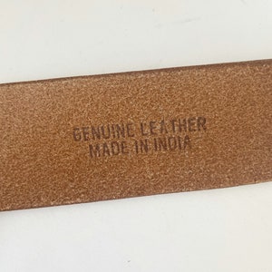 May include: Close-up of a brown leather belt with the text "GENUINE LEATHER MADE IN INDIA" embossed on the back.